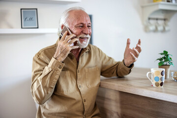 Senior man drinking morning coffee at his domestic kitchen and using phone. Elderly bearded man drinking coffe in the kitchen and having fun while making phone call.
