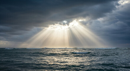 Dramatic dark sky with sunlight breaking through the clouds, creating powerful crepuscular rays over the vast ocean