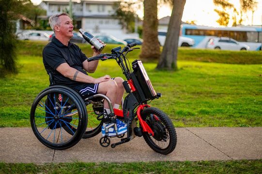 Individual on an adaptive electric bike relaxes and drinks in a park setting during sunset