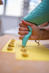 Close up shot of a hand expertly piping filling onto fresh pasta dough creating homemade ravioli in a bright kitchen setting