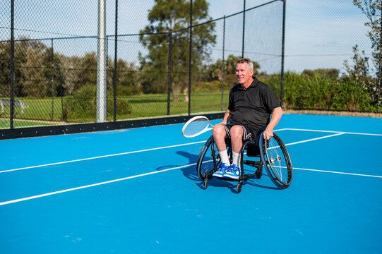 Male athlete practices wheelchair tennis on an outdoor court during a sunny day