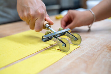 Homemade pasta making close up shot of hands using a pasta cutter to slice fresh dough into uniform...