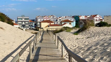 Wooden boardwalk through sand dunes leading to colorful striped houses in Costa Nova, Aveiro, Portugal, famous tourist destination, traditional Portuguese architecture