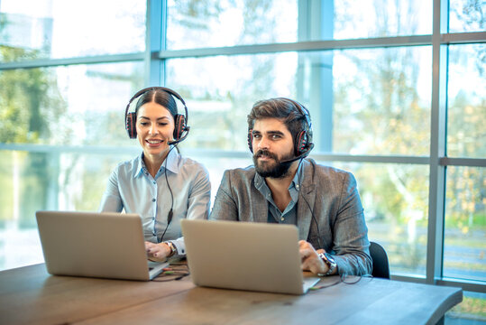 Male and female call center agents working together on laptops assisting clients in office