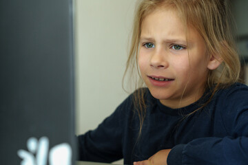 A girl sits at her computer, confuzed, studying. She frowns and ponders, unable to comprehend what's on the screen.