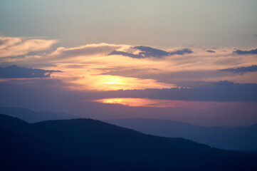 Clouds in sky at evening above hills. Beautiful view of landscape in mountains, sun sitting in summer. Concept of beauty of nature and harmony.