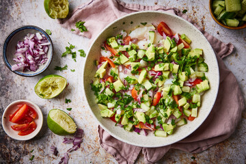 Mexican aguachile (ceviche) on a plate with napkin in the background and limes and fresh herbs