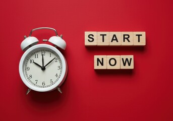 An alarm clock and wooden blocks with the words START NOW on a red background