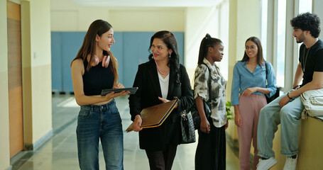 Indian young adult female busy lady tutor hold file walk indoor campus place use tablet look screen do online work teen girl pupil discuss study talk new plan share idea learn casual e skill