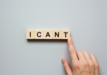 A hand pointing at the word ICANT on wooden blocks on a gray background