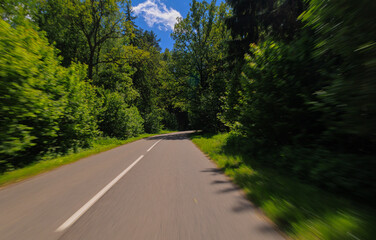 Road in the countryside, roadside and asphalt, green forest and fields, blue sky and clouds	
