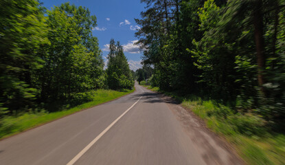 Naklejka premium The effect of speed on the road and blurred objects. View of the road on a sunny summer day.