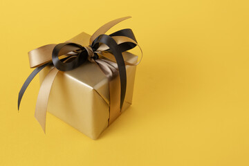 Golden gift box with black and golden ribbon on yellow background, space for text