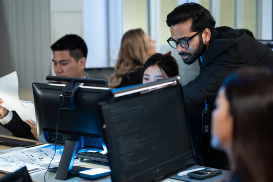 Indian IT manager providing mentorship and hands-on guidance to a diverse colleage working on a computer code. Technical training, team leadership, and active collaboration in software development