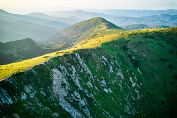 Aerial view of rugged mountain range with lush green slopes at sunset. Landscape showcases beauty of untouched nature with distant peaks and valleys bathed in soft sunlight. Carpathians, Chornogora.