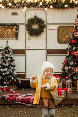 little girl looks up and waits for the first snow and celebrates Christmas near the trailer with Christmas decorations