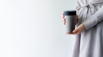 Young Woman in Silver-Gray Dress with Steaming Travel Coffee Tumbler, Solid White Studio Background, Modern Advertising Minimalism