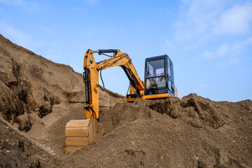 Obraz premium Construction site on a sunny day. Industrial excavator digging sand to lay the foundation for a building. Workers operate the excavator.