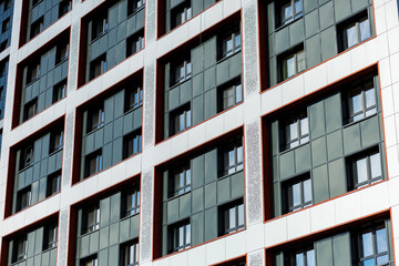The building's façade features a contemporary design, featuring a curtain wall. White panels alternate with textured inserts, and the windows are framed in red, creating a striking accent.