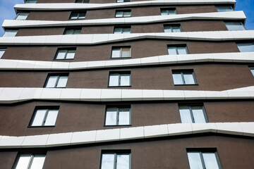 Obraz premium The residential complex's façade features a contemporary design with wavy white elements contrasting with the brown background. Large windows add light and a cozy feel.
