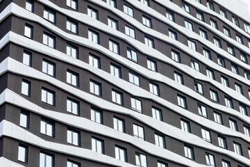 A modern residential complex with a wave-shaped fa&ccedil;ade, finished in dark tones with white accents. The architecture emphasizes dynamism and style, creating a unique appearance.