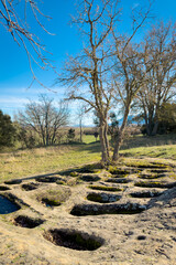 Ground-level view of the San Andres necropolis in Villarcayo, Burgos, Spain. The image shows medieval rock-cut tombs carved directly into stone, surrounded by natural vegetation and rural landscapes