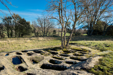 Ground-level view of the San Andres necropolis in Villarcayo, Burgos, Spain. The image shows medieval rock-cut tombs carved directly into stone, surrounded by natural vegetation and rural landscapes
