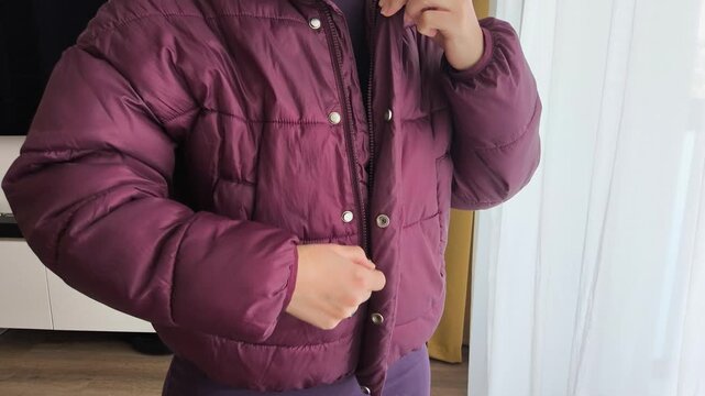 Individual in a purple puffer jacket is engaged in zipping up the front, showcasing the action of fastening outerwear in a bright indoor setting with natural light