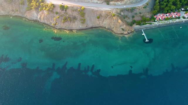 aerial footage capturing the scenic coastal road and turquoise waters along the Dat&ccedil;a Peninsula, leading towards the historic Knidos Ancient City in Turkey. Perfect for travel
