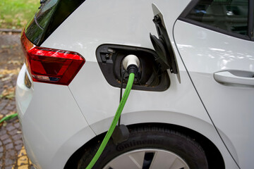 Electric vehicle charging with green cable connected to the rear of a modern white car in a natural setting