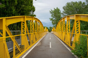 Yellow metal bridge spans over a road surrounded by lush greenery and mountains in the background with copy space