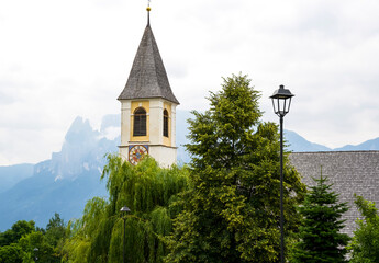 Historic church tower with clock surrounded by lush greenery and mountains in the background showcasing natural beauty
