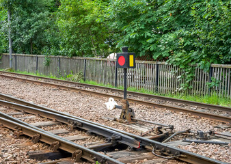 Railway signal with red and yellow lights beside train tracks in a lush green environment with copy space