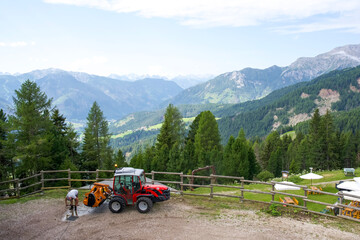 Red tractor parked on mountain landscape with worker preparing equipment in scenic alpine environment