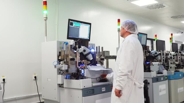 Employee of high-tech microchip factory monitors printing press. Microchip production equipment is in operation. Engineer at workstation. Modern equipment for printing microchips and circuit boards.