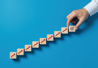 Hand arranging wooden blocks with rising arrows towards a target on a blue background from a top view