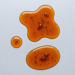 A Top-Down Close-Up of Honey-Colored Liquid Puddles with Entrapped Bubbles on a Minimalist Gray Surface, Evoking Texture, Depth, and Surface Tension.