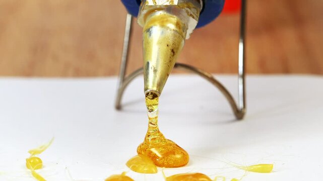 A blue hot glue gun melting yellow glue onto white surface, creating textured pattern. glue appears glossy and vibrant, with strands extending from nozzle, showcasing creativity and craft