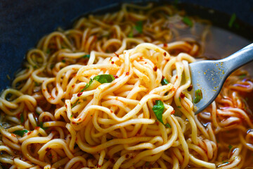 Instant noodles on fork in a bowl. Spicy noodle soup. Asian food style.