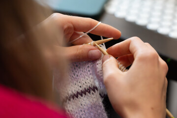 closeup of young female hands knitting a warm scarf with wool yarn and bamboo needles