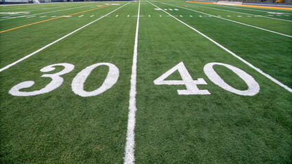 An American football field, showcasing a meticulously maintained green grass surface, marked with white yard lines and numbers