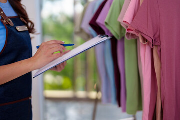 Asian adult hands manage colorful apparel inventory checking stock in a vibrant boutique shop