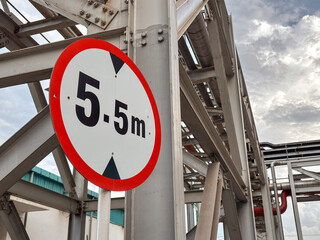A round height restriction sign of 5.5 meters stands against a steel structure under sky.