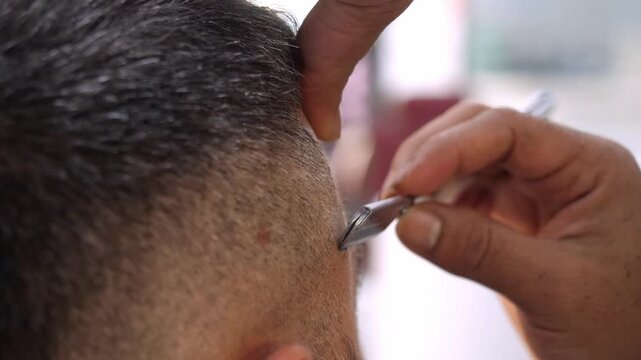 Close-up of barber using razor blade on client hair in salon
