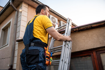 Worker climbs ladder for roof maintenance in residential area during sunny afternoon