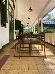 Quiet cafe porch with dark wood furniture and classic white pillars. Indonesia/Southeast Asia colonial architecture detail. Relaxing outdoor dining area.