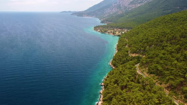 An aerial view captures the stunning natural beauty of G&ouml;kova Bay in Turkey, showcasing the vibrant turquoise waters meeting a pristine coastline backed by dense, verdant forests and rolling hills. Th