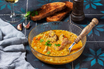 Lentil soup with pork and vegetables, served with white wine and croutons.