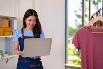 Asian woman small business owner managing online clothing store using laptop from home for digital commerce