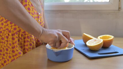 Woman squeezing fresh orange juice with a manual juicer at home. Close-up of hands pressing orange, preparing healthy vitamin drink in the kitchen - Powered by Adobe
